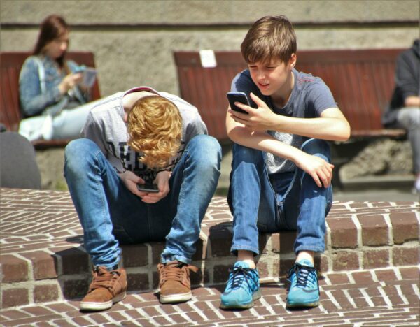 twee jongens van ongeveer vijftien jaar zitten beiden op een stop naast elkaar op hun mobiele telefoon te kijken.