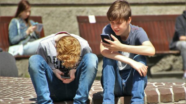 twee jongens van ongeveer vijftien jaar zitten beiden op een stop naast elkaar op hun mobiele telefoon te kijken.