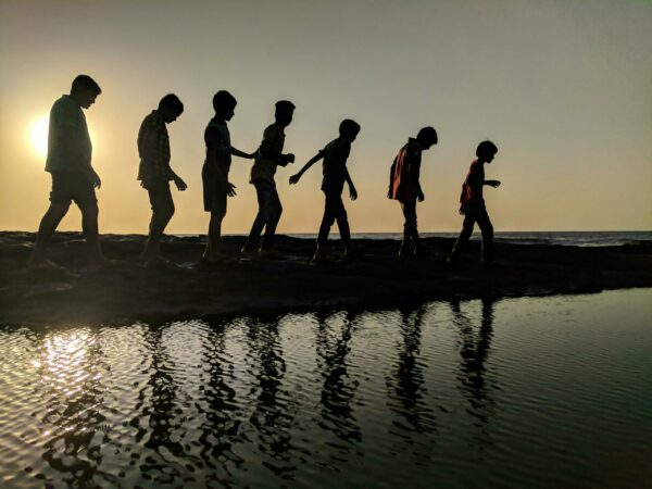 7 personen van groot naar klein die langs het water lopen tijdens zonsondergang