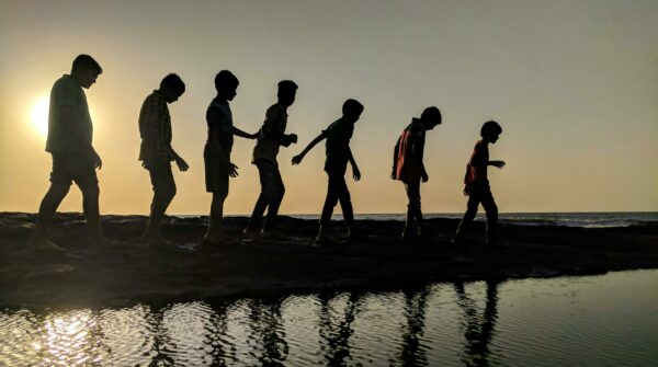 7 personen van groot naar klein die langs het water lopen tijdens zonsondergang