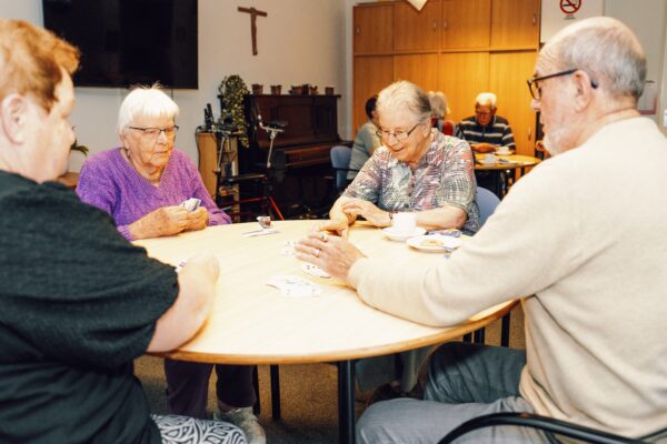 4 ouderen mensen die aan een ronde tafel een kaart spel aan het spelen zijn.