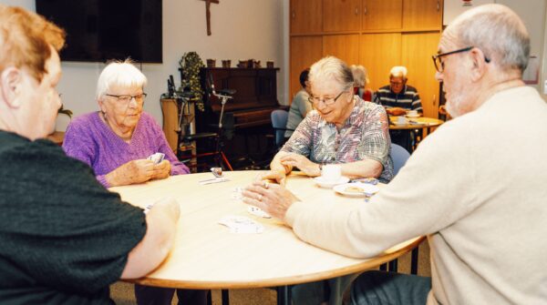 4 ouderen mensen die aan een ronde tafel een kaart spel aan het spelen zijn.