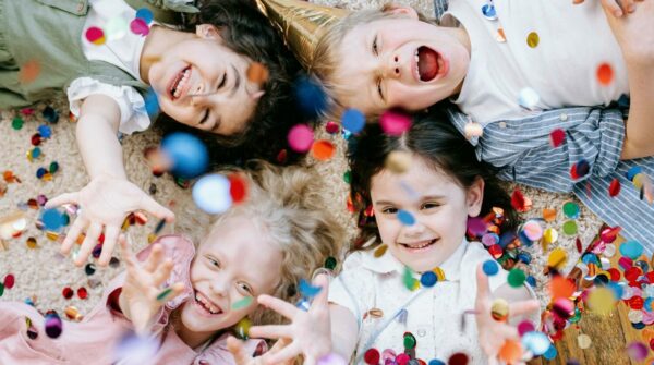 Vier kinderen liggend op de grond die confetti in de lucht gooien